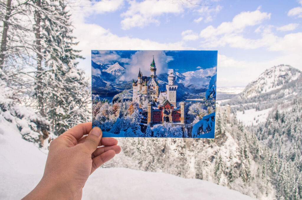 Postcard being held in front of Neuschwanstein castle in the winter