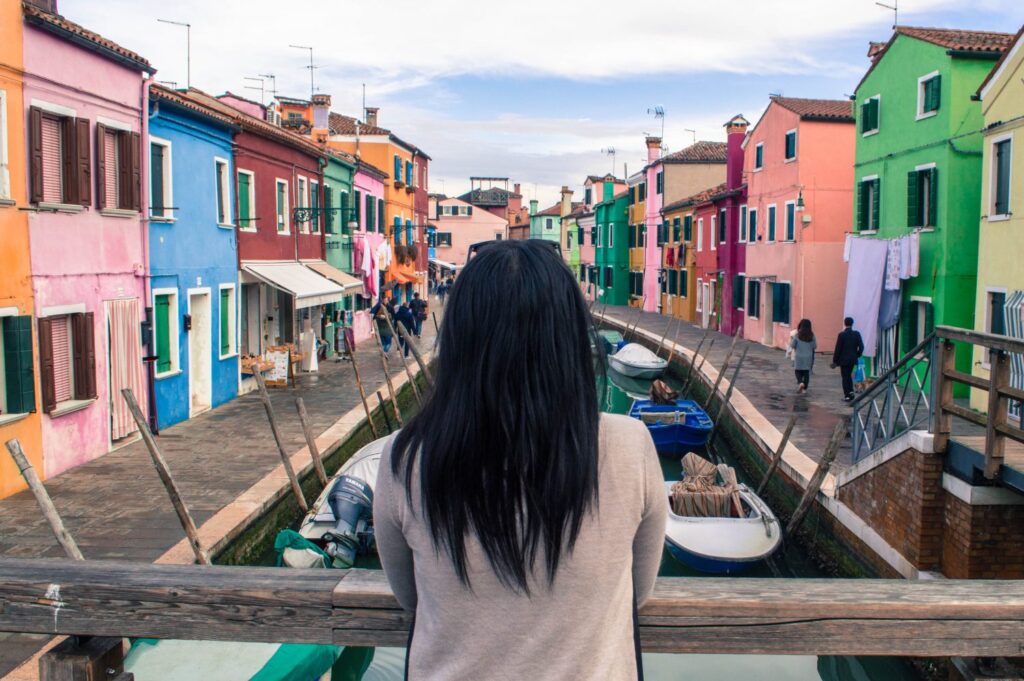 Girl posing with rainbow houses in Burano Italy on a bridge