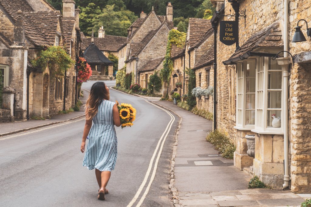 Travel blogger Christina Guan from Happy to Wander walking along the main street of Castle Combe, England.