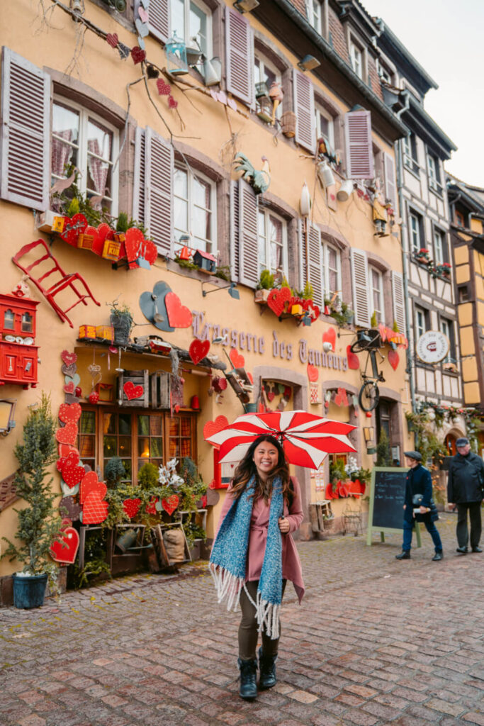 Travel blogger with a red and white umbrella in front of a restaurant in Colmar, France