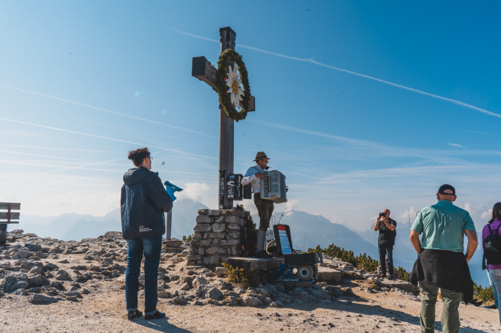 Cross on top of Eagle's Nest in Munich with a performer playing accordion surrounded by spectators