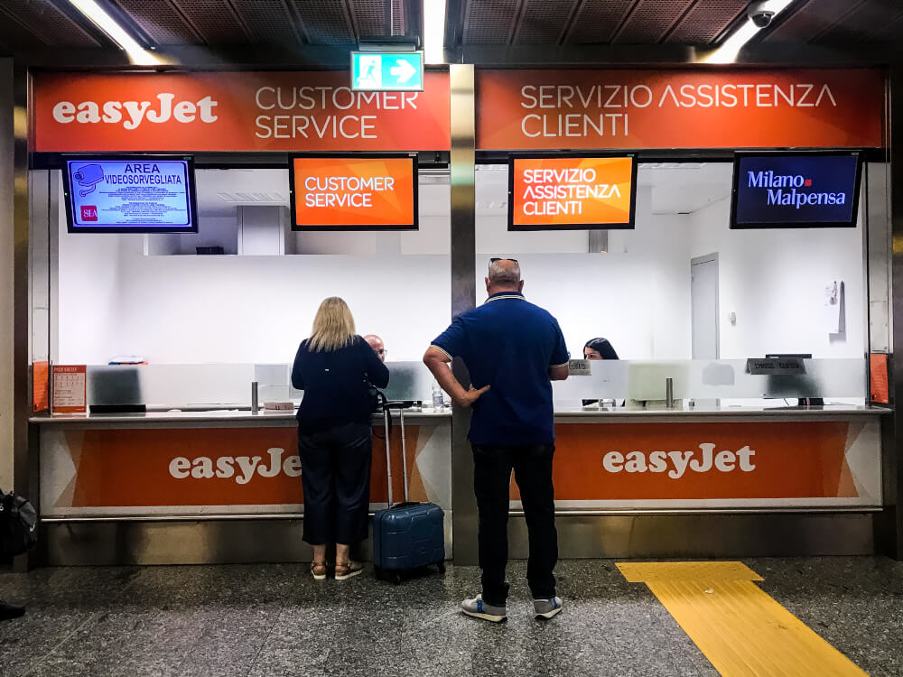 Two passengers standing at an easyJet customer service desk in Milan Malpensa airport