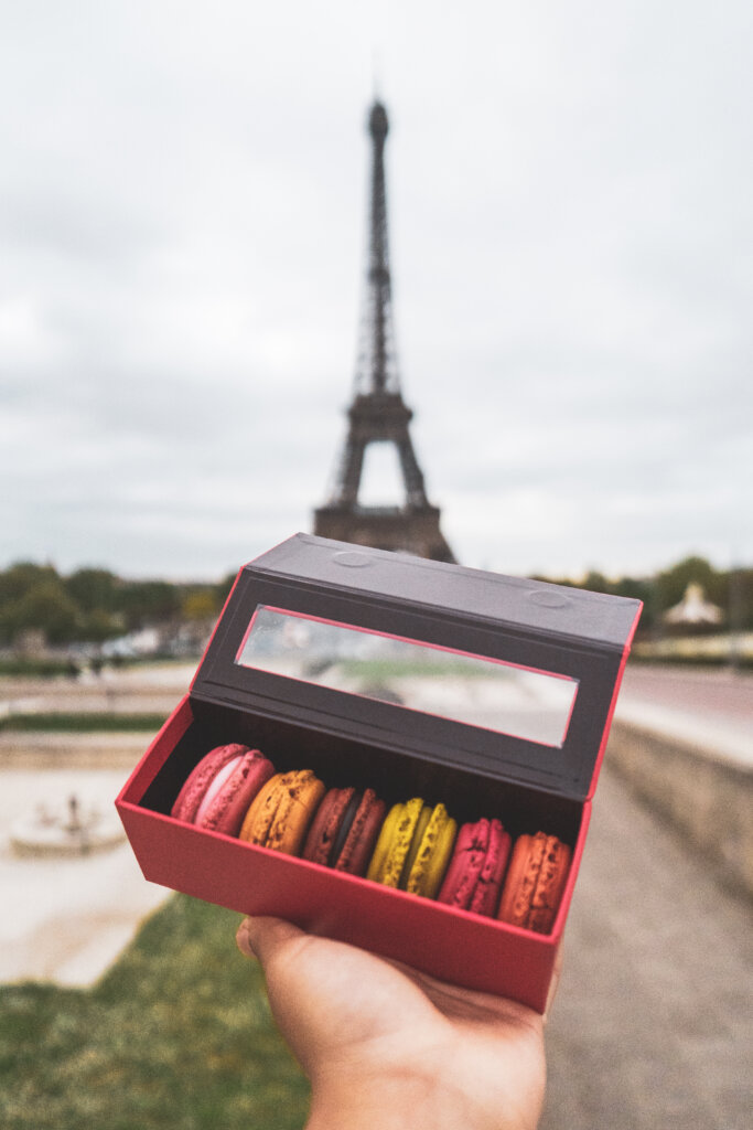 Colourful macarons held out in front of the Eiffel Tower