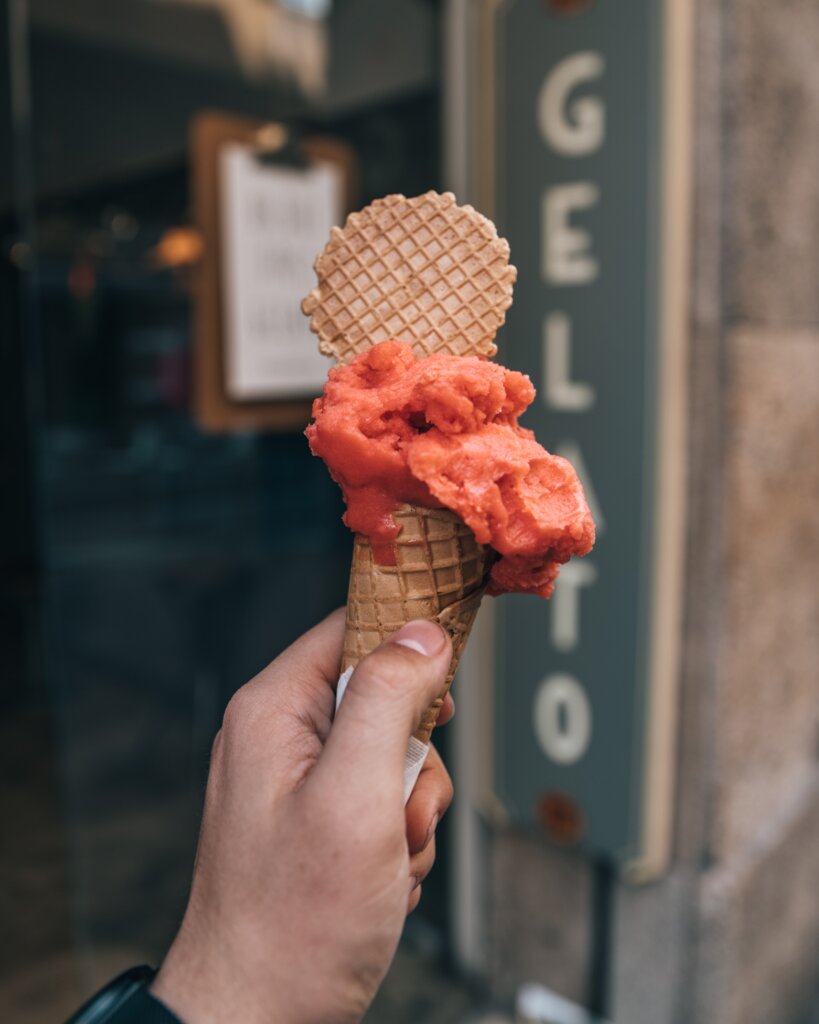 Berry gelato in a waffle cone in front of a shop in Italy