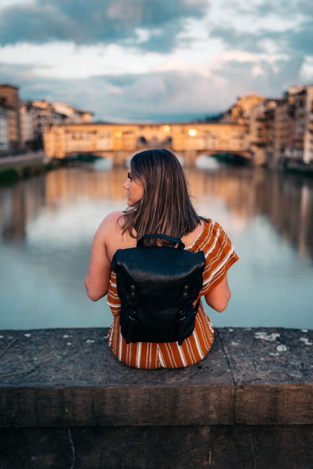 Girl in an orange dress and black backpack sitting at a scenic view in Florence