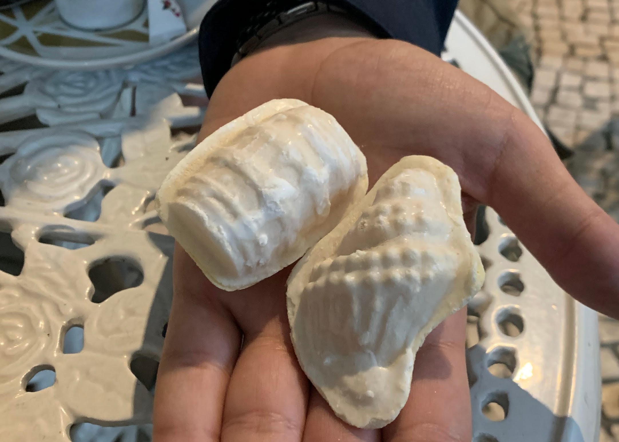 A hand holding two small white pastries that are shaped like a barrel and a shell