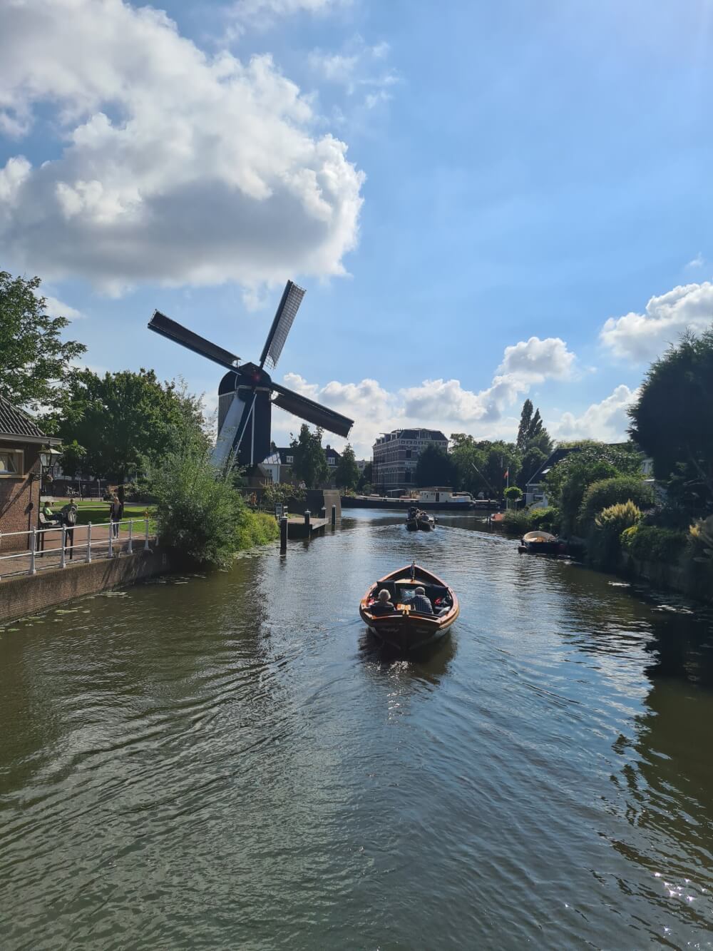 A small boat on a canal with a windmill on the banks on a sunny day.