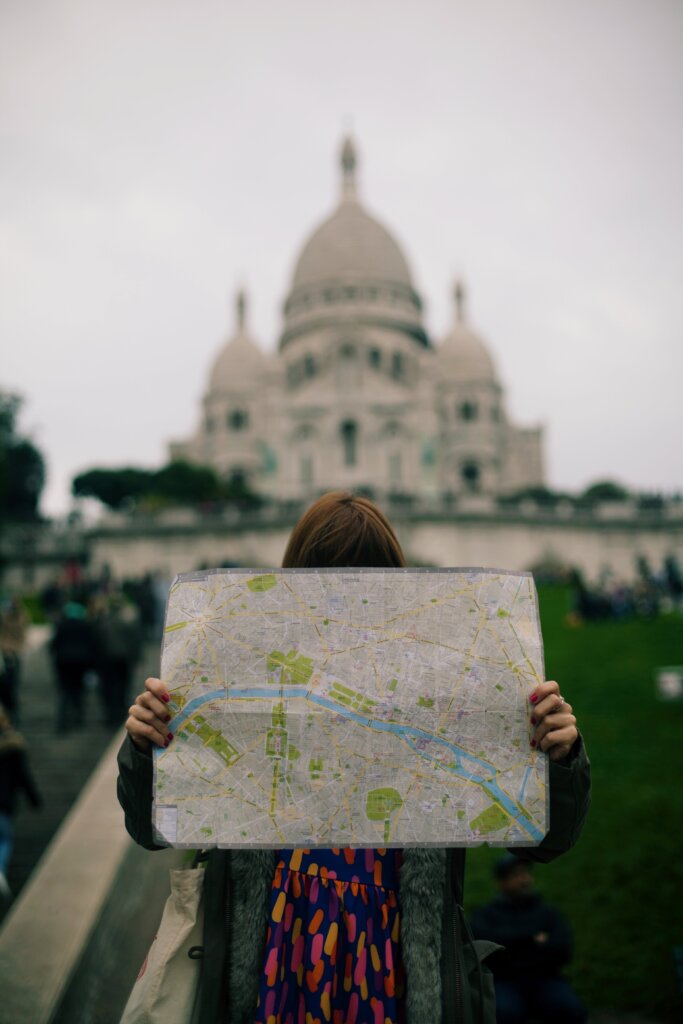 Girl holding map in front of her face in front of the Sacre Coeur Basilica in Paris, France