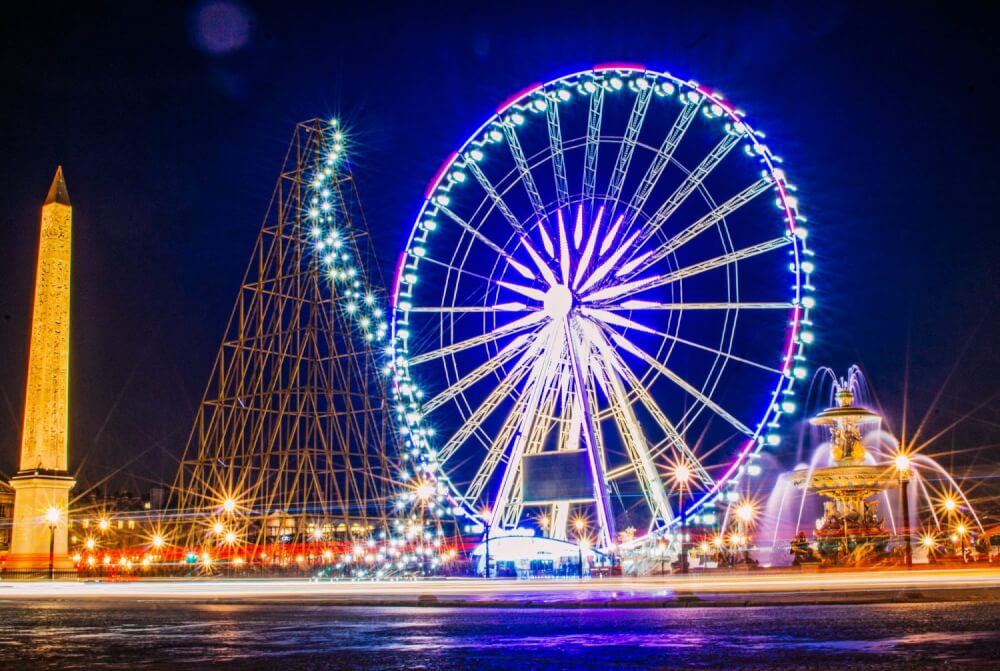 Night time scene in Paris, with a giant ferris wheel and tree made of lights