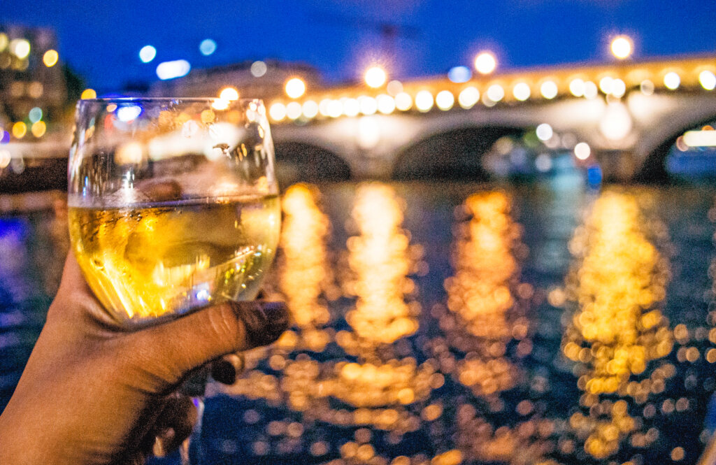 Glass of white wine being held out in front of the Seine River