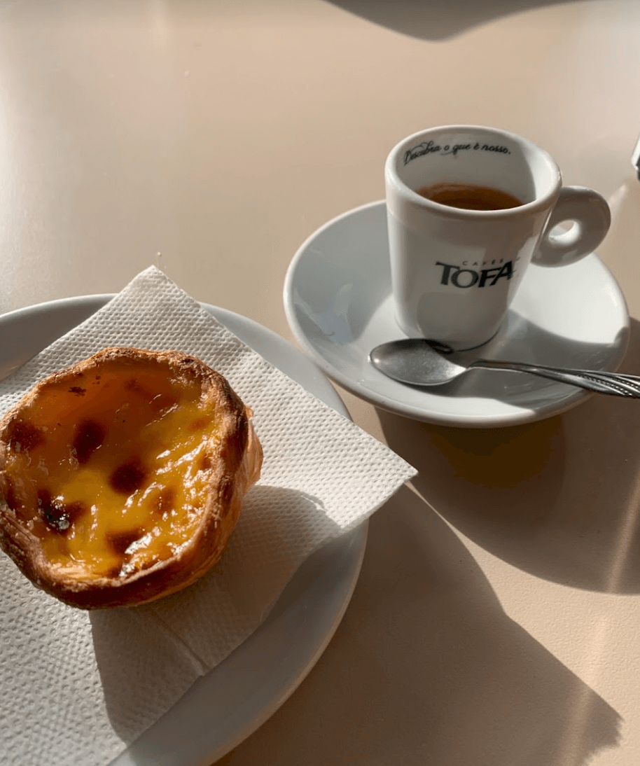 A table topped with an espresso, spoon, and small custard pastry