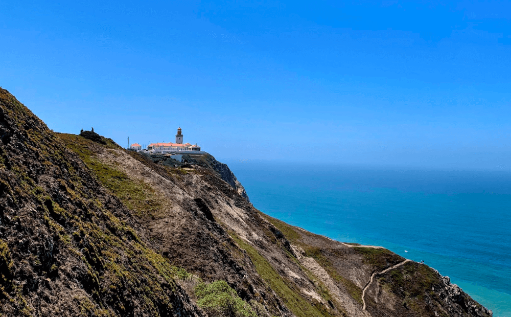 A lighthouse perched high on a cliff on a sunny day. 