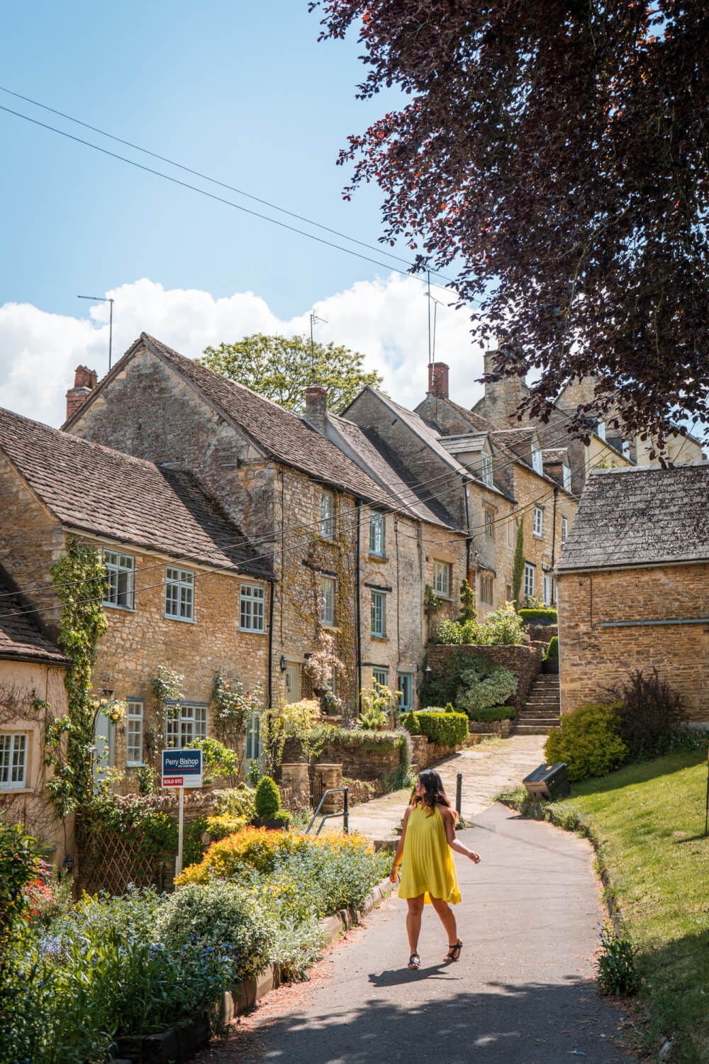 Christina Guan from Happy to Wander in front of beautiful Cotswolds brownstone cottages.