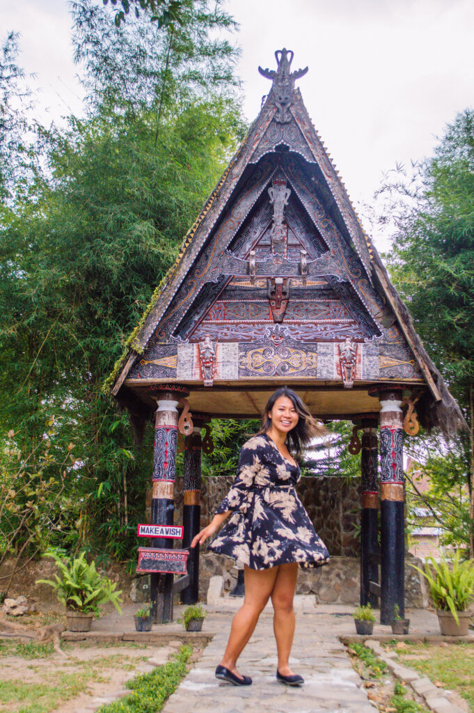 Girl in a dress twirling at Lake Toba in front of a traditional house