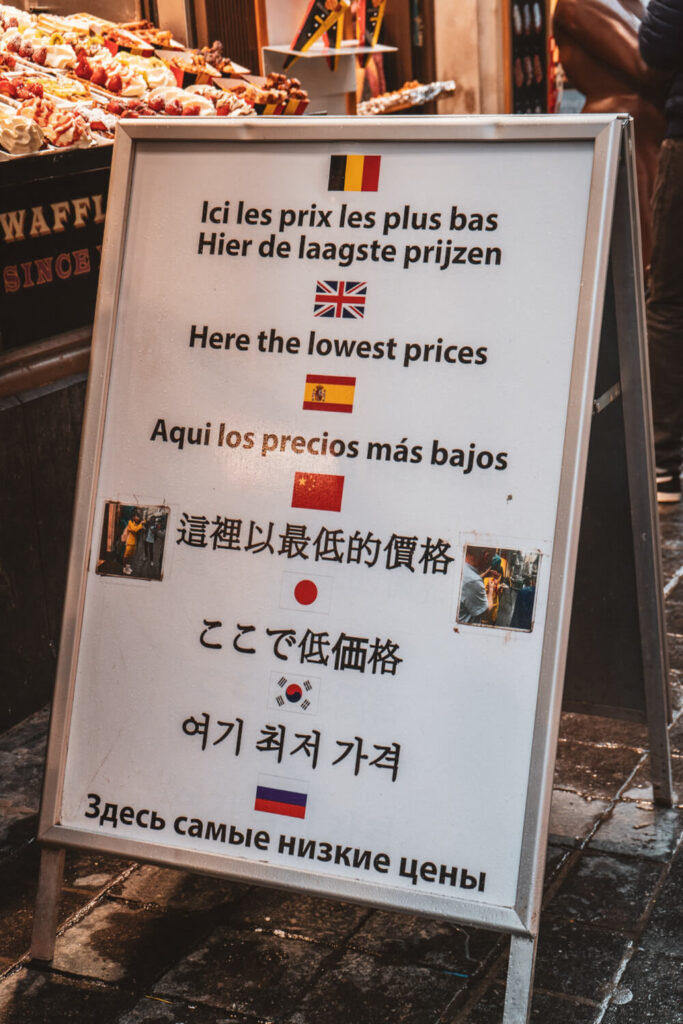 Sign in Brussels city center with multiple languages saying they have the cheapest prices for waffles