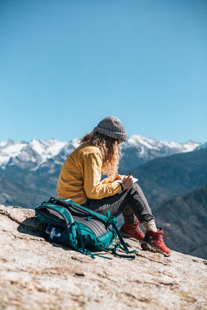 Woman in a yellow jacket writing on top of a mountain