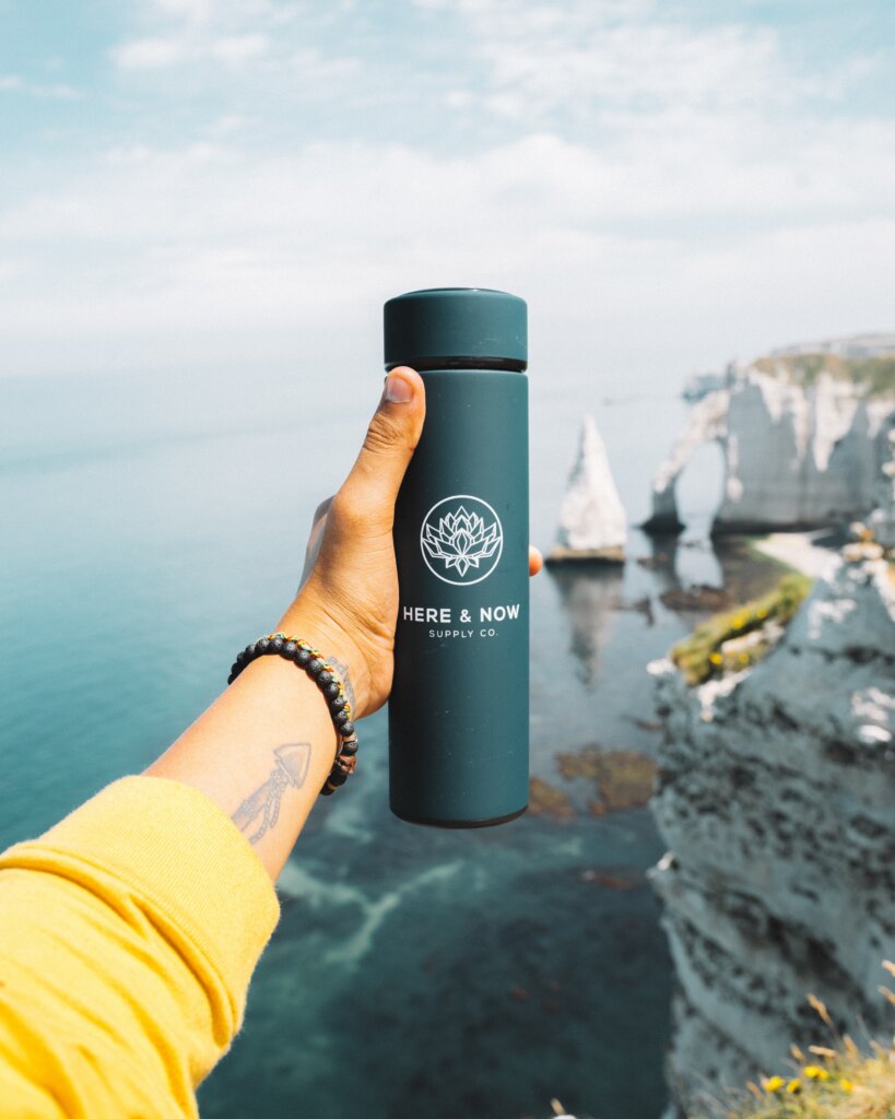 Traveler with a tattoo holding out a water bottle in front of a scenic view 