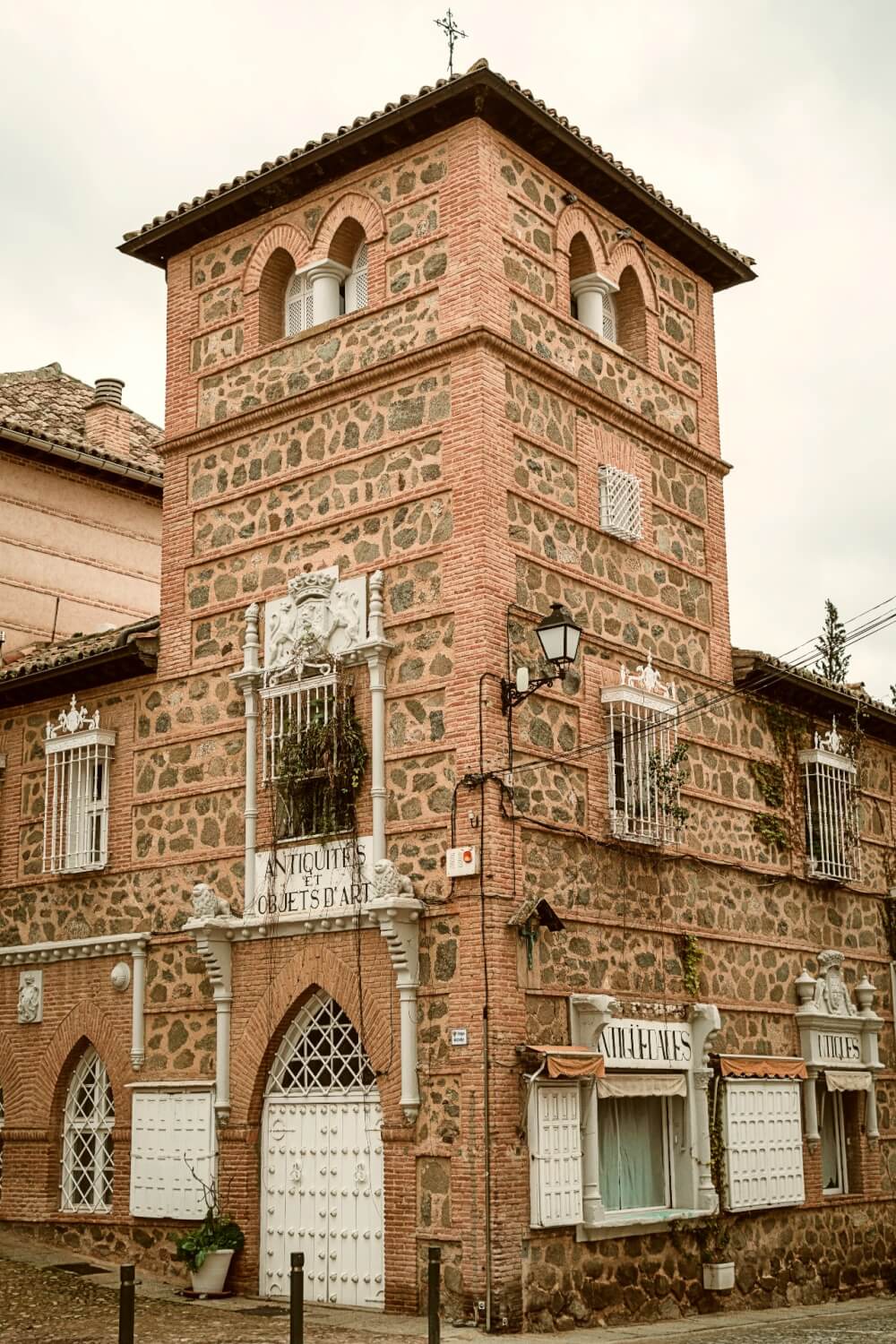 A square stone tower with arched doors and windows. The sigh out front is in French, and translates to "Antiques and works of art"