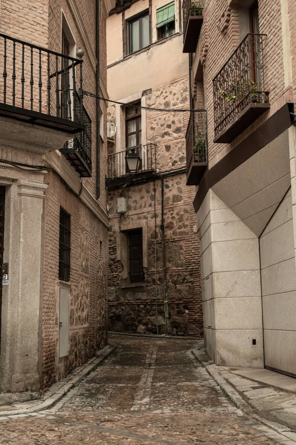 Narrow street in Toledo. The buildings that line the street are all made of stone, and have small balconies on the first story.