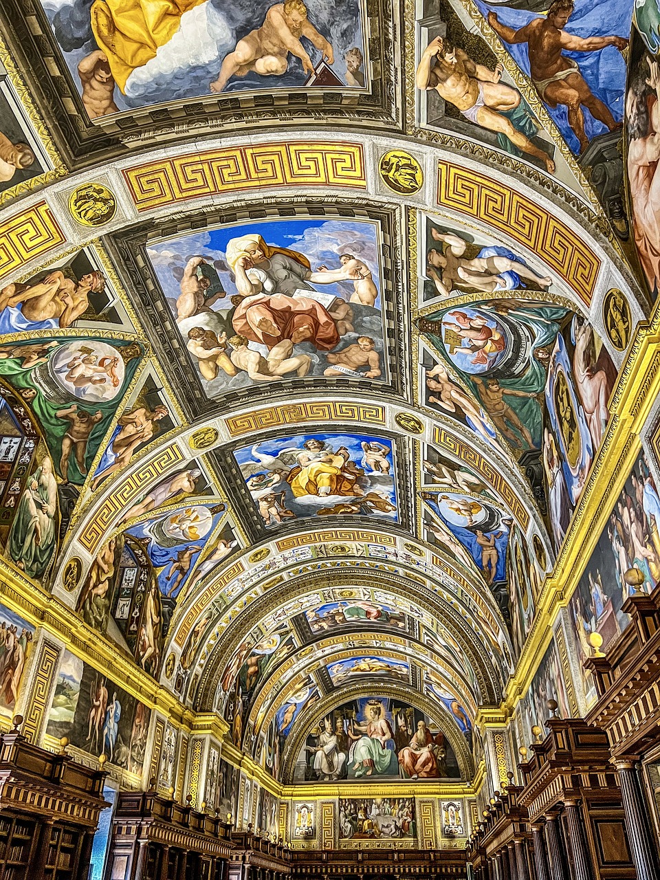 A domed ceiling in a library with bright blue, gold, and green religious paintings