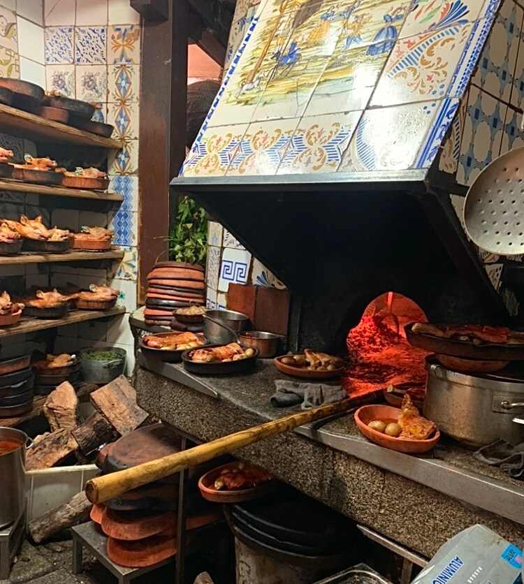 Plates of chicken and pork being cooked in an old fashioned, tile-decorated oven