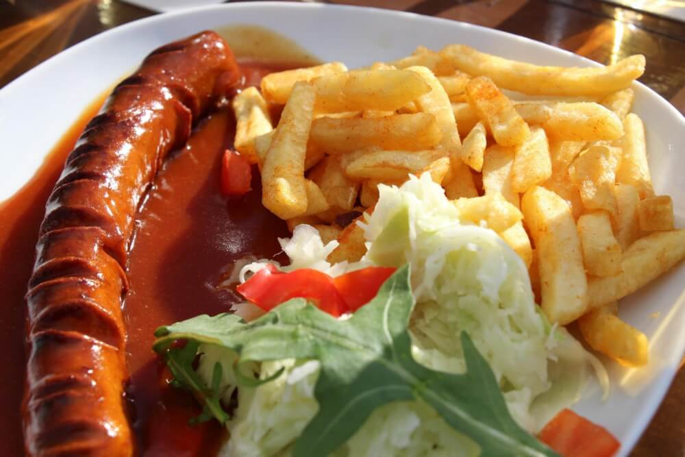 Currywurst on a plate with fries and a salad.