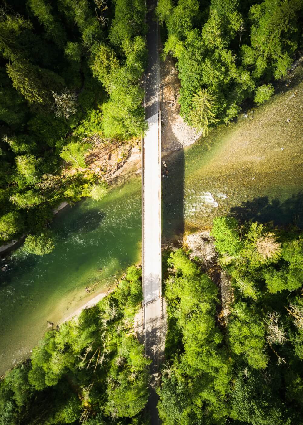 A view of a bridge crossing a river on a sunny day, with lush vegetation on both sides.