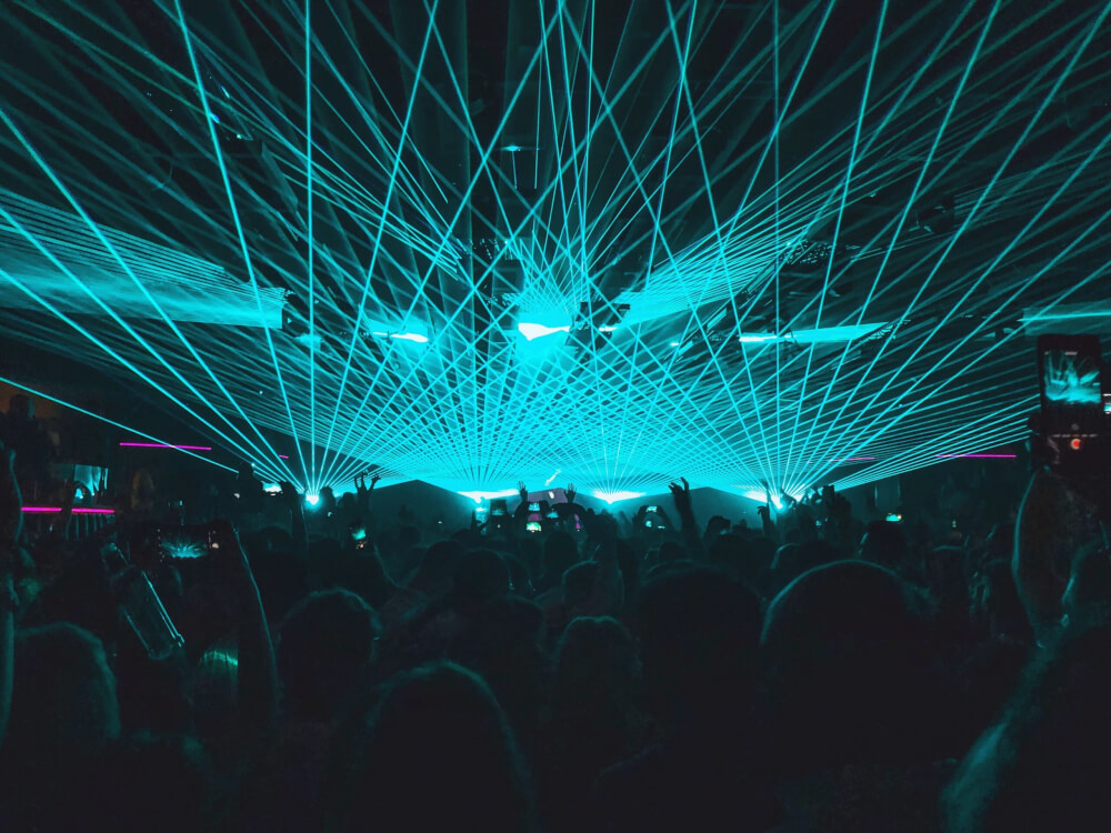 People dancing at a nightclub, with blue laser lights going across the ceiling. 