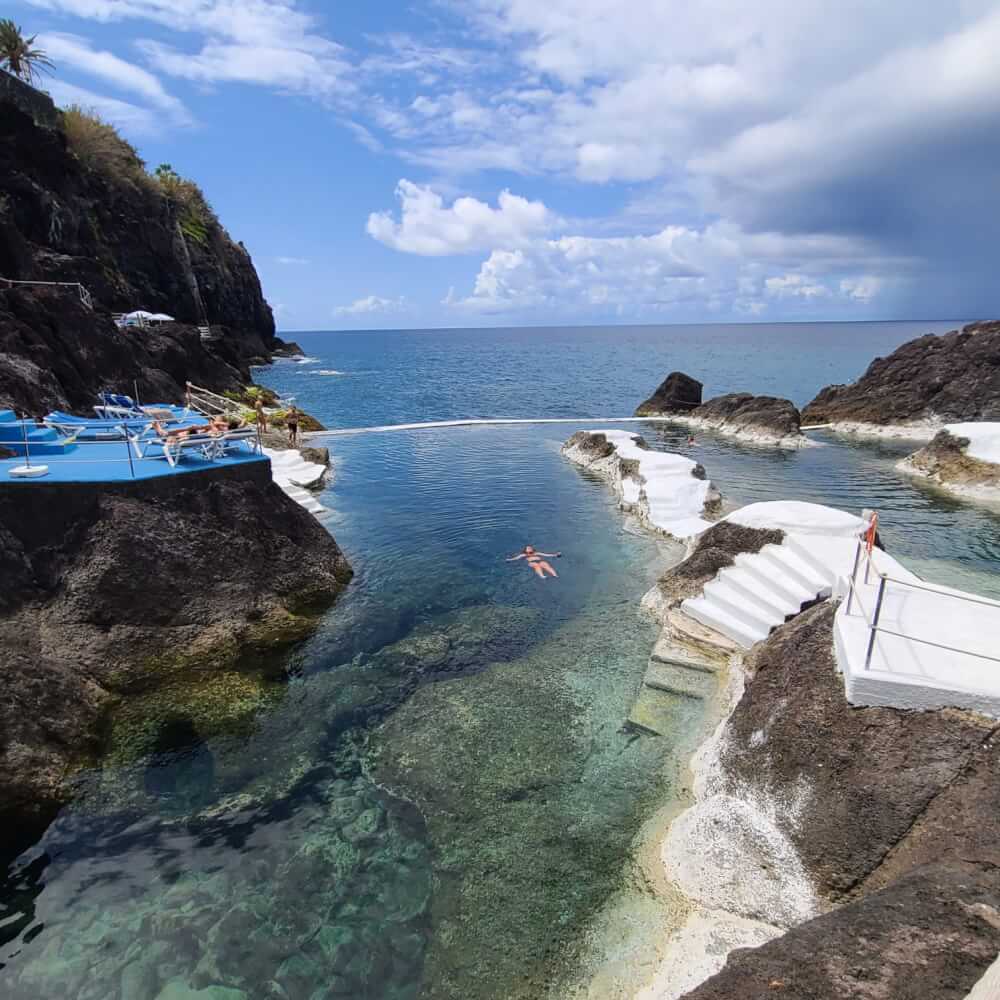 A woman floating in a natural volcanic pool. Another person is sleeping in a lounge chair.