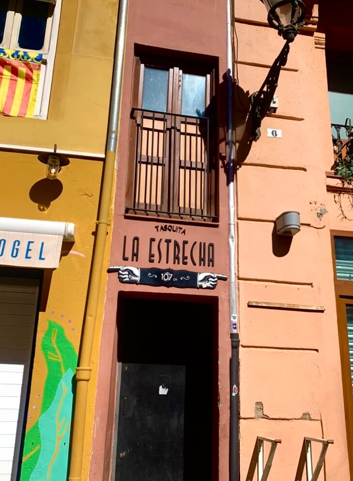 A narrow, red facade with a sign that says "La Estrecha, 107 cm" 