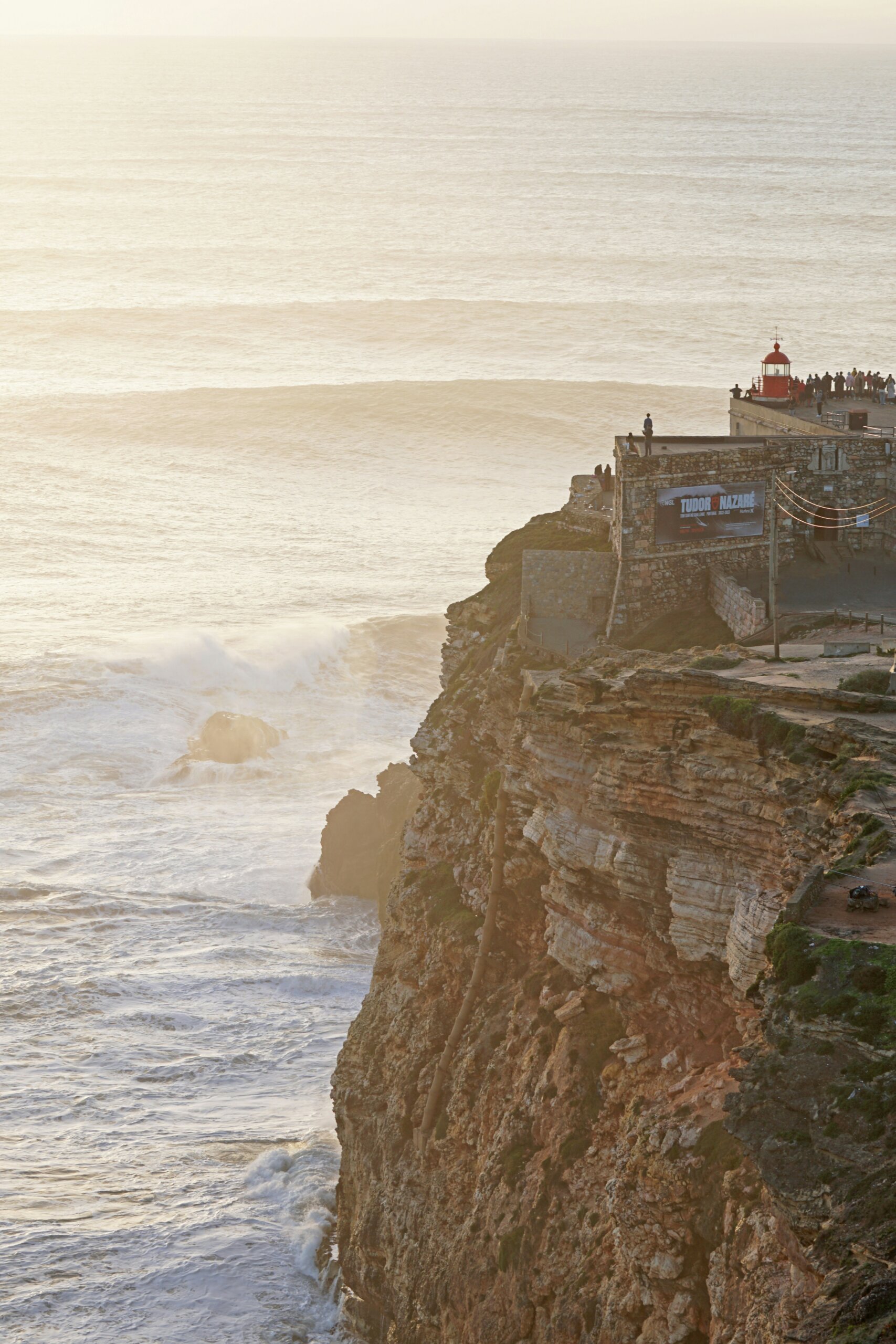 A group of people standing near a light house looking at the ocean