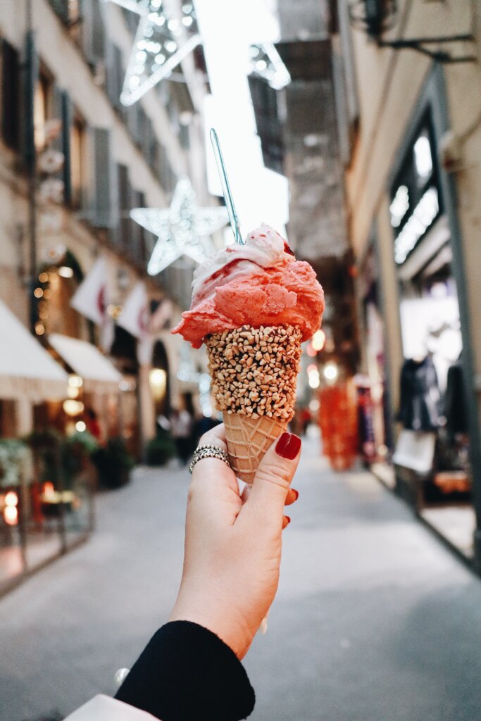 Girl with red nails holding out pink gelato in front of street