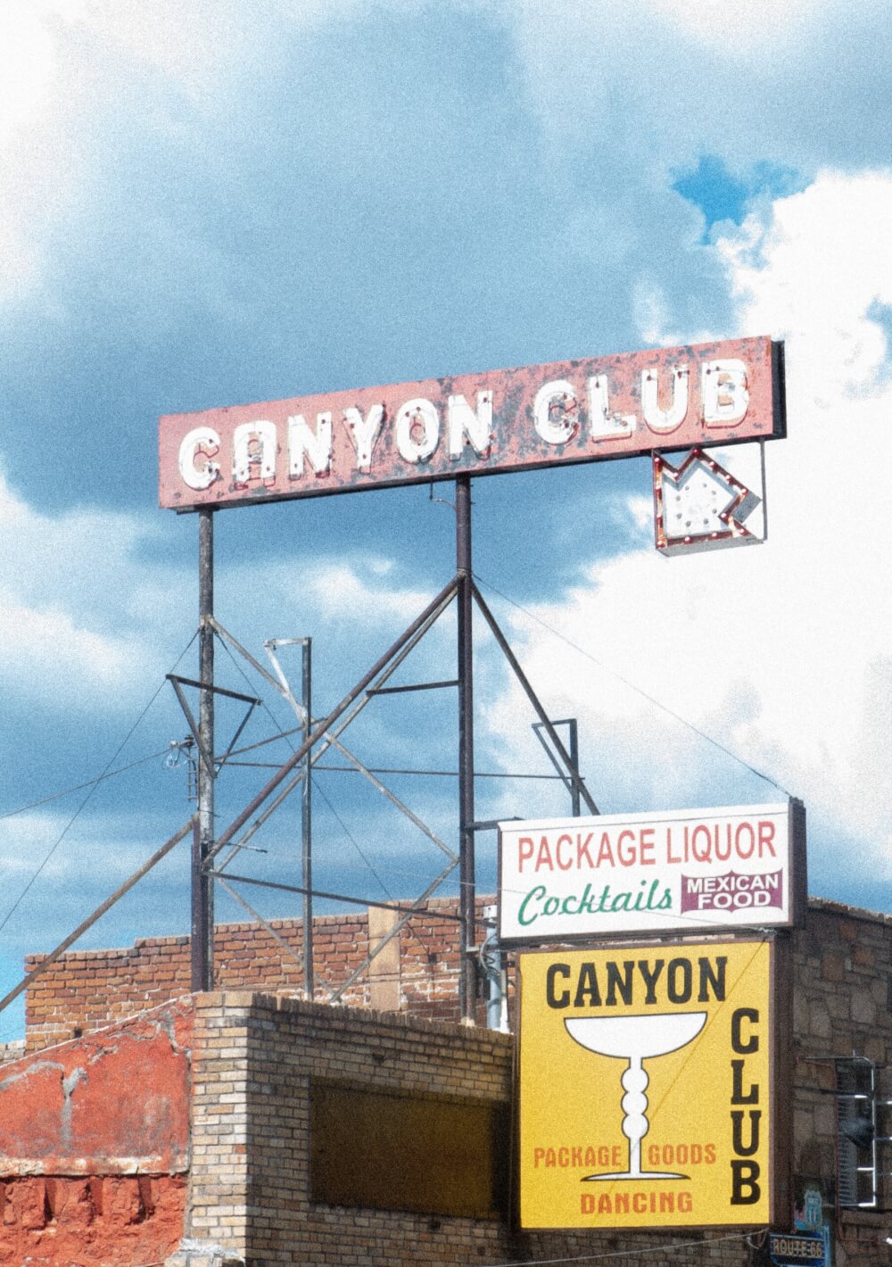 The side of a building with different signs advertising a liquor store, Mexican food, and a bar on a hot day with a blue sky. 