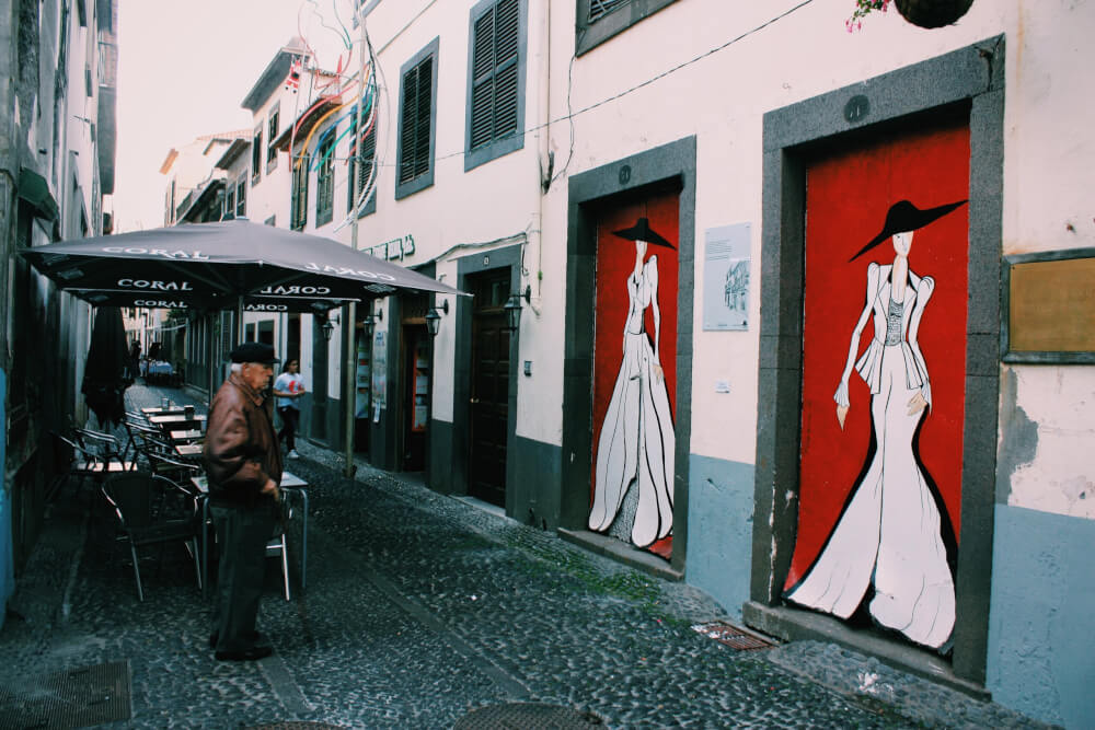 A city street where two doors have been painted. The painting is a black and white silhouette of a woman in a black hat, against a red background.