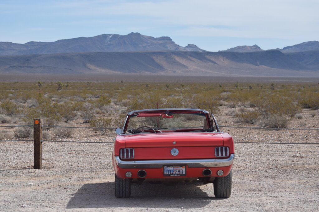 A red car parked in front of an arid, desert expanse of land.