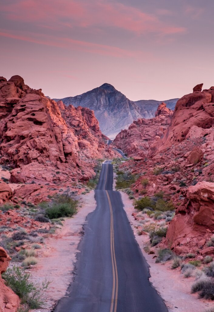 A highway cutting through mountain foothills as the sun sets. 