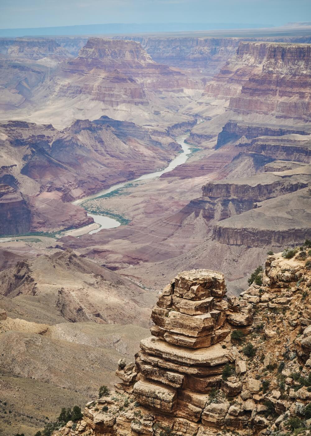 A view of a river cutting through the grand canyon at midday, providing the full scope of the hazardous terrain mules have to traverse. 