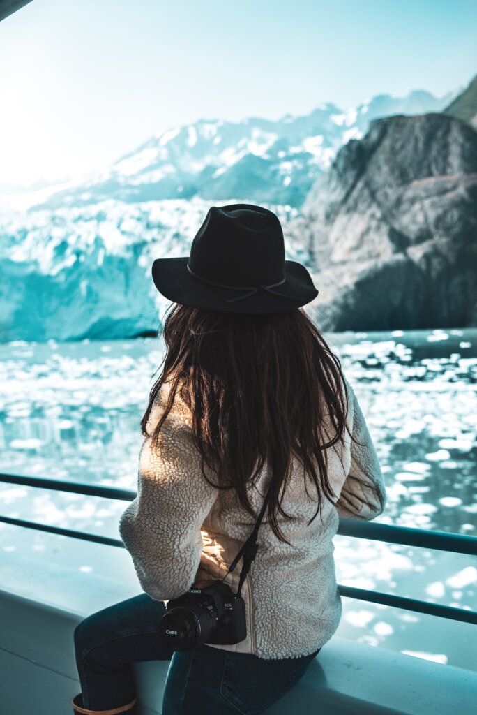 A woman with a hat on a ferry in Alaska, marveling at a glacier. 