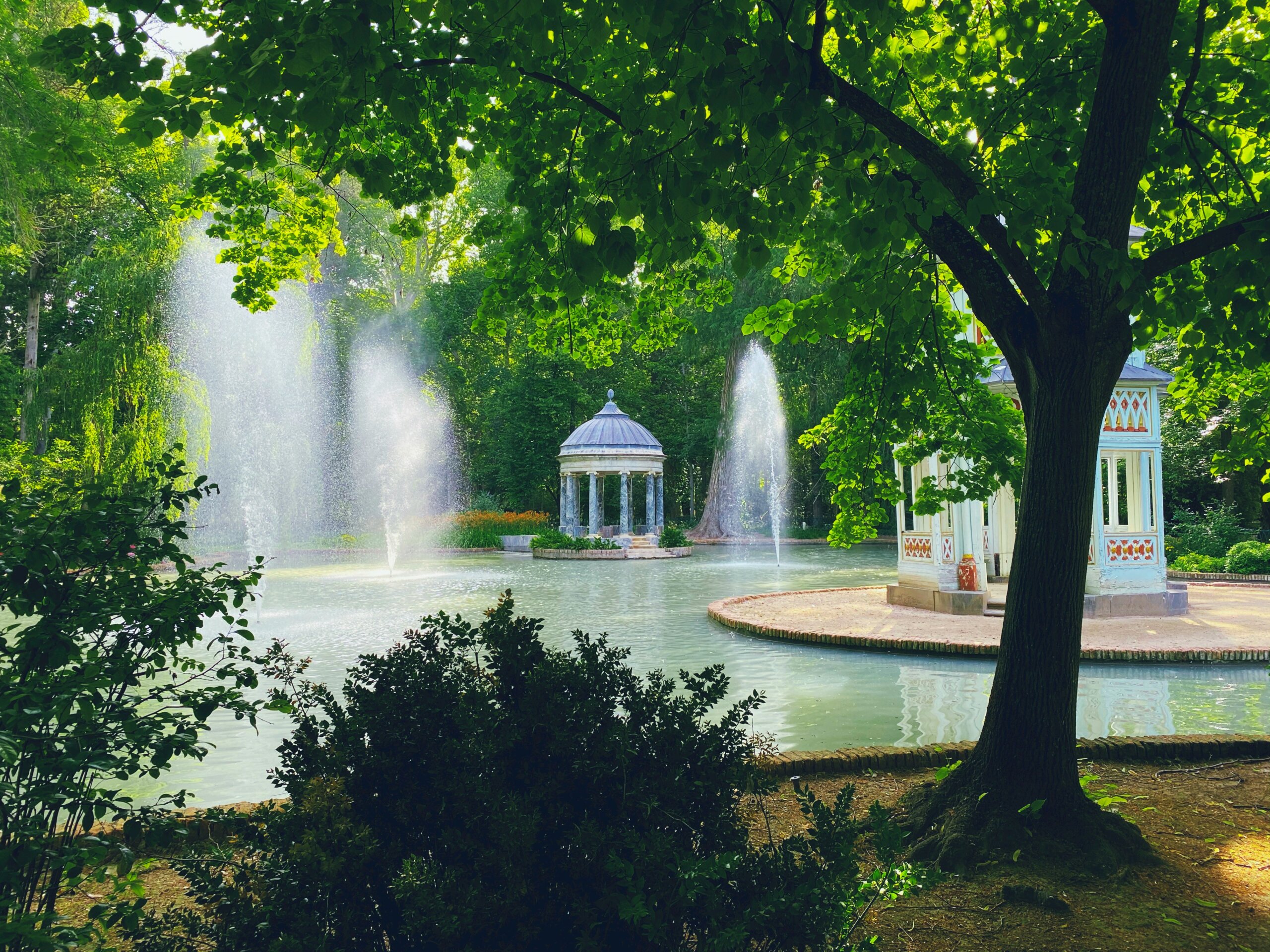 A lake with fountains next to two gazebos