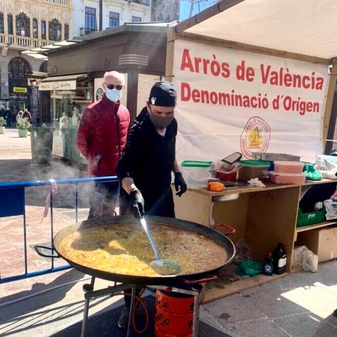 Man stirs rice over a large paella pan at an outdoor food festival