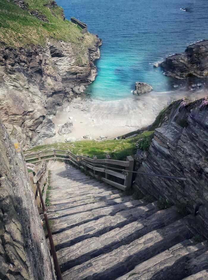 A steep walkway leading down to a turquoise water beach in Cornwall, England.