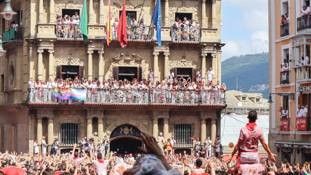 Crowds of people cheering in the streets and in balconies at the festival. Most people are wearing matching white and red outfits.