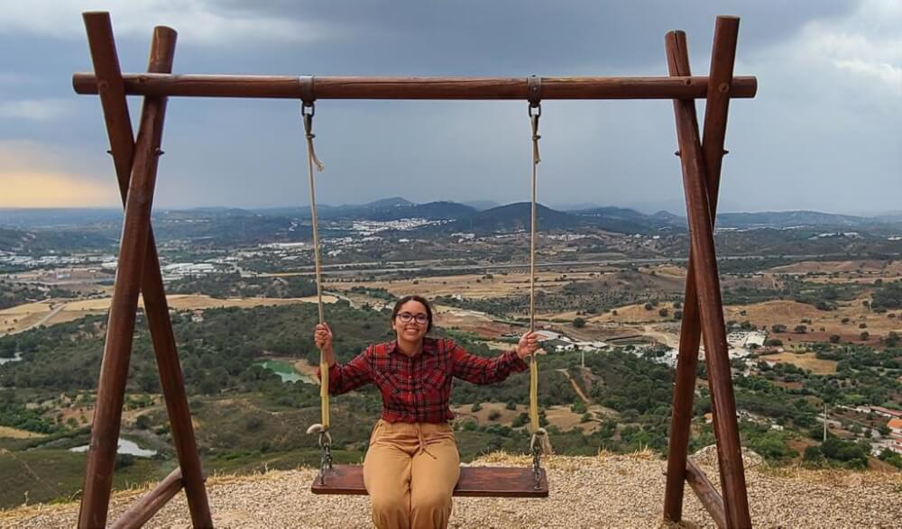 Person sitting on a swing in front over a valley