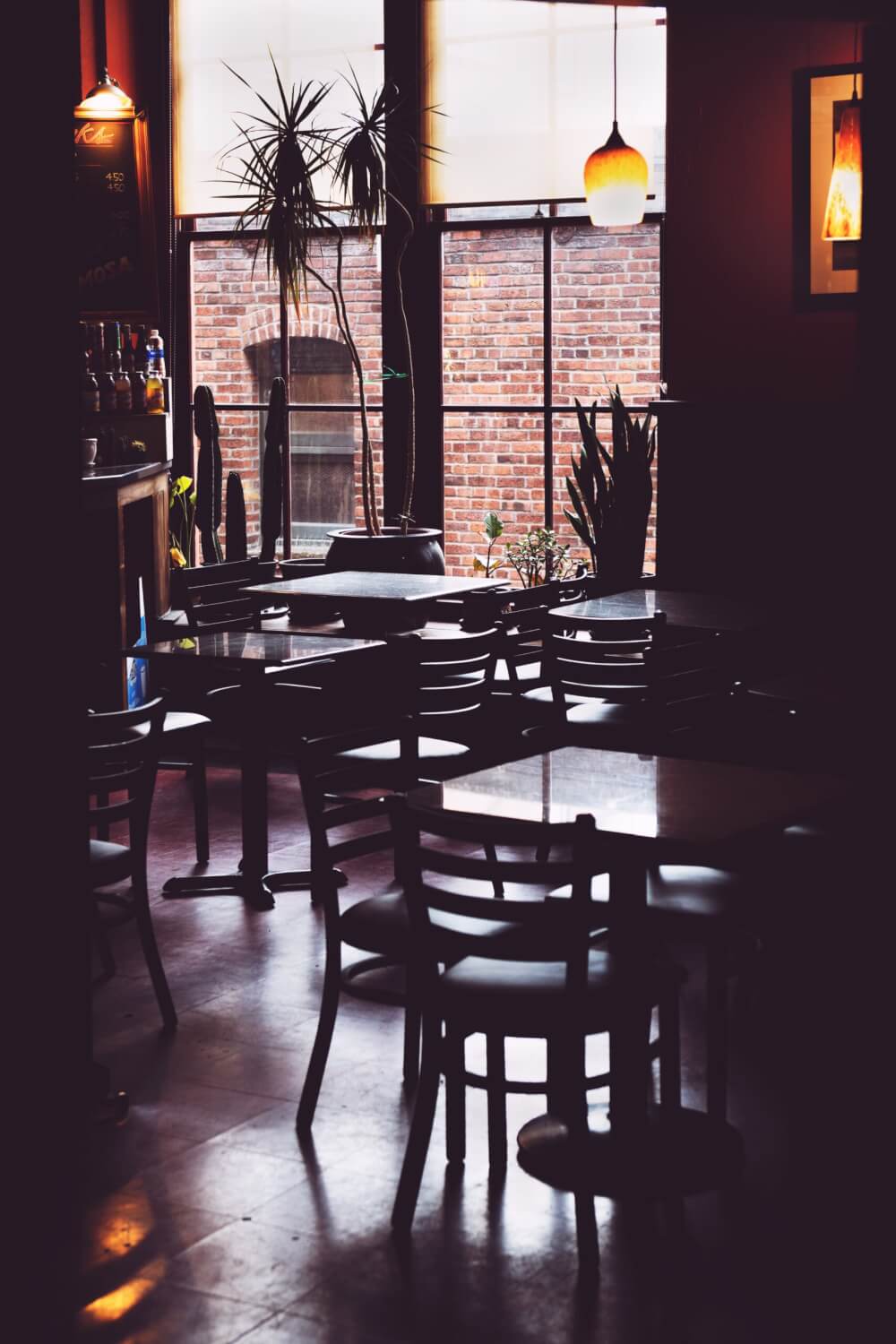 A view of an empty cafe, with a brick wall outside its window and the lights turned off. 