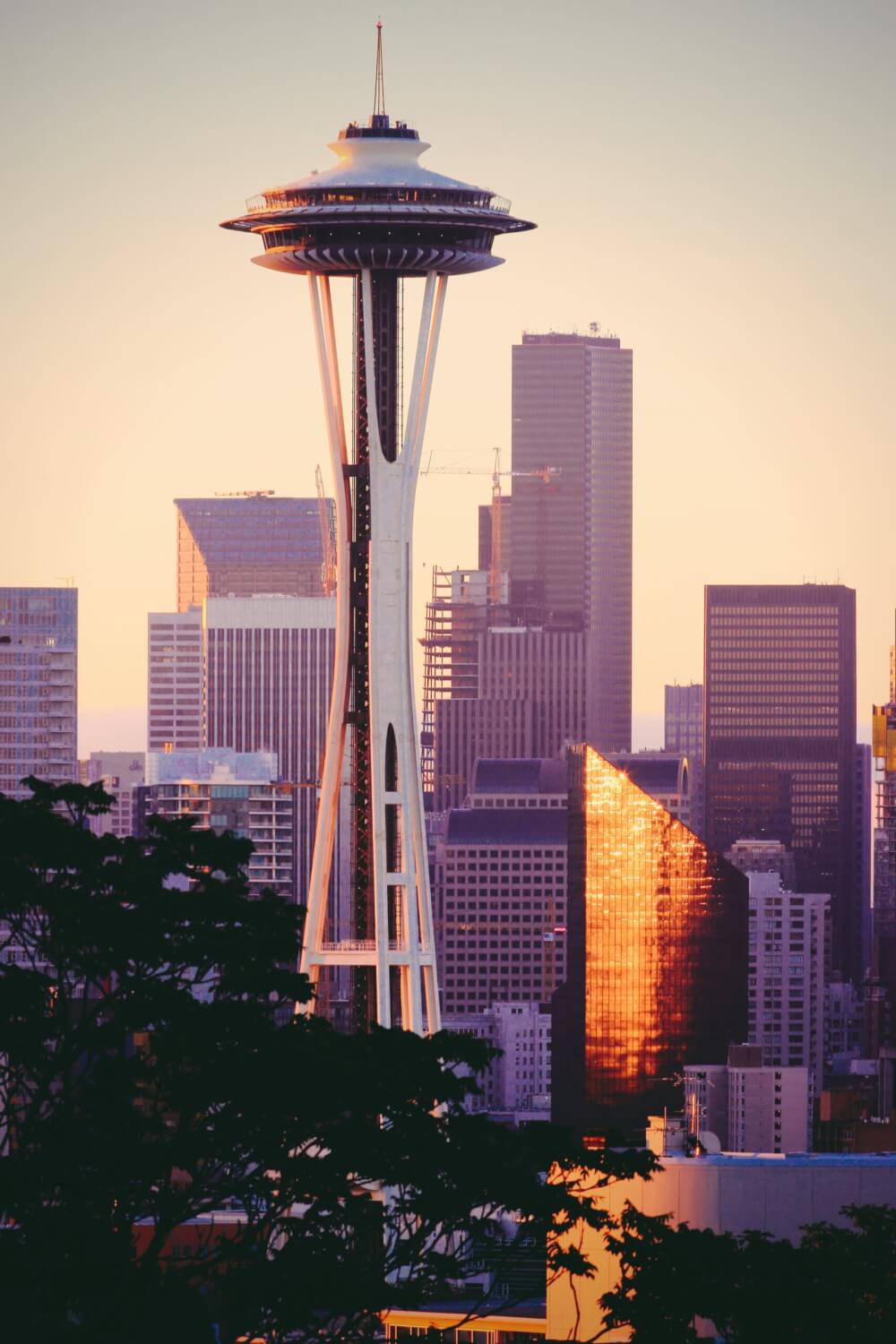 The towering Space Needle at dusk with skyscrapers, cranes, and other buildings in the background.