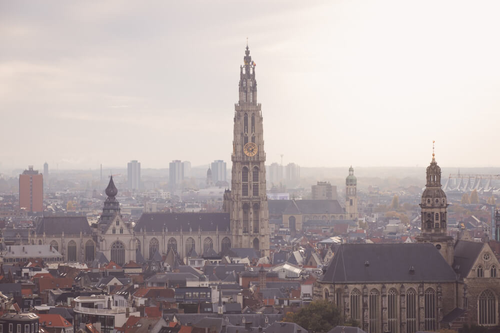 Aerial view of Antwerp Cathedral towering over the city on a hazy day.